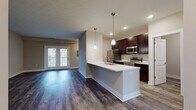 Located at 4663 Crystal Ball Dr. in Hilliard, Ohio, this single-floor residence offers a thoughtfully designed open-concept layout with contemporary finishes throughout. The kitchen serves as a central hub of the space, showcasing rich dark cabinetry, light quartz countertops, a large peninsula island with an undermount sink, and a full suite of stainless steel appliances including a refrigerator, range, and microwave. Pendant lighting above the island adds a modern touch, while recessed ceiling lights provide even illumination across the space. The kitchen flows seamlessly into the living area, which features dark hardwood-style flooring and a set of French doors that invite natural light and provide outdoor access. The bedrooms are carpeted for comfort, with one featuring a walk-in closet outfitted with wire shelving. The primary bathroom includes a soaking tub and shower combination, dark vanity cabinetry, and light countertops, while a second bathroom offers a standalone walk-in shower. Wood-look flooring carries through the bathrooms, maintaining a cohesive aesthetic. Neutral wall tones and clean white trim throughout create a bright, versatile backdrop well-suited to a variety of interior styles.