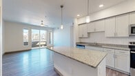 This well-appointed 3-bedroom, 3-bathroom single-floor residence offers a thoughtfully designed open-concept layout finished with consistent wood-style flooring throughout. The kitchen serves as a central hub of the home, showcasing a large granite-topped island with pendant lighting, crisp white shaker cabinetry, stainless steel appliances including a refrigerator, range, and microwave, and a dishwasher — all tied together by a clean, modern aesthetic. The kitchen flows seamlessly into the living areas, one of which features sliding glass doors opening to a private balcony with outdoor views, complemented by a ceiling fan overhead.

The three bedrooms are bright and generously proportioned, with large windows inviting natural light and views of the surrounding neighborhood. The primary bedroom includes its own dedicated bathroom. The bathrooms are uniformly finished with granite-topped white vanities, large mirrors, and wood-style flooring; one features a soaking tub and shower combination, while another offers a walk-in shower stall. A hallway connects the private rooms and includes access to an in-unit laundry area. The overall ambiance is clean, contemporary, and move-in ready, reflecting a cohesive modern design throughout.