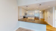 Located on the 20th floor in the heart of Charlotte, NC, this one-bedroom, one-bathroom unit offers a well-designed layout with modern finishes throughout. The open-concept kitchen is a standout feature, equipped with stainless steel appliances including a refrigerator with ice maker, electric range, and built-in microwave. White flat-panel cabinetry extends to the ceiling, complemented by a gray quartz peninsula countertop, tile backsplash, and globe pendant lighting — all set atop warm hardwood flooring that flows through the main living area. The bedroom offers comfortable carpeting underfoot, a ceiling fan, and a large window framing sweeping city views of the Charlotte skyline — a notable highlight of this high-floor residence. A dedicated closet provides practical storage. The bathroom is finished with floor-to-ceiling white tile in the tub/shower combo, a wide vanity mirror with overhead lighting, and a dark quartz countertop with an undermount sink and white cabinetry. Soft, neutral tones and clean lines are consistent throughout, creating a cohesive and contemporary ambiance. The unit is efficiently laid out, making excellent use of its footprint while maintaining a light, airy feel enhanced by recessed lighting and large windows.