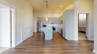 Located at 201 S Main St in Owasso, Oklahoma, this well-appointed 2-bedroom, 2-bathroom residence offers a thoughtfully designed single-level layout with a clean, contemporary aesthetic. The open-concept kitchen serves as a central highlight, featuring gray shaker-style cabinetry extending to the ceiling, a large center island with a white quartz countertop, stainless steel appliances, and elegant pendant lighting — all set above rich hardwood-style flooring that carries through the main living areas. The two bedrooms are carpeted for comfort, each offering a dedicated closet with built-in shelving and rod storage. Large, black-framed windows allow natural light to fill the rooms while providing views of the surrounding Owasso cityscape. The primary bathroom is appointed with large-format neutral tile flooring, a floating vanity with a white countertop, and a glass-enclosed soaking tub and shower combination with accessibility-friendly grab bars. The second bathroom maintains the same refined palette with a floating vanity, tile flooring, and a well-lit mirror. Neutral tones, clean lines, and modern fixtures are consistent throughout, giving the space a cohesive and polished feel suited for comfortable everyday living.