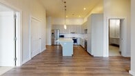 Located at 201 S Main St in Owasso, Oklahoma, this well-appointed 2-bedroom, 2-bathroom residence offers a thoughtfully designed single-level layout with a clean, contemporary aesthetic. The open-concept kitchen serves as a central highlight, featuring gray shaker-style cabinetry extending to the ceiling, a large center island with a white quartz countertop, stainless steel appliances, and elegant pendant lighting — all set above rich hardwood-style flooring that carries through the main living areas. The two bedrooms are carpeted for comfort, each offering a dedicated closet with built-in shelving and rod storage. Large, black-framed windows allow natural light to fill the rooms while providing views of the surrounding Owasso cityscape. The primary bathroom is appointed with large-format neutral tile flooring, a floating vanity with a white countertop, and a glass-enclosed soaking tub and shower combination with accessibility-friendly grab bars. The second bathroom maintains the same refined palette with a floating vanity, tile flooring, and a well-lit mirror. Neutral tones, clean lines, and modern fixtures are consistent throughout, giving the space a cohesive and polished feel suited for comfortable everyday living.