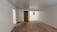 Located at 2435 Maple Valley Hwy in Renton, WA, this single-floor unit offers a practical and straightforward layout across a modest footprint. The living area is finished with neutral-toned carpet and white walls, creating a clean, understated atmosphere. A built-in shelving niche adds a subtle architectural detail, while a wood-paneled interior door provides a warm contrast to the otherwise light interior. The space benefits from natural light filtering through window blinds, contributing to a bright and open feel.

The bedroom is a well-proportioned private retreat, finished with the same neutral carpet and white walls. A window allows for natural light and ventilation, and a flush-mount ceiling light fixture provides functional overhead illumination.

The kitchen features warm wood cabinetry with brass hardware arranged above and below a laminate countertop with marble-like veining. A stainless steel drop-in sink anchors the workspace, offering practical utility in a compact setting.

The bathroom includes a wood-toned vanity with a white countertop, a large mirror, tile flooring, and accessibility-oriented grab bars near the toilet. Adjacent built-in shelving provides additional storage. Overall, the unit presents a functional, no-frills design suitable for efficient everyday living.