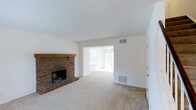 This two-story residence offers a well-organized layout across two floors, providing distinct living and sleeping zones for added comfort and privacy. The main level features a spacious living room highlighted by a classic brick fireplace with a natural wood mantel, serving as a charming focal point of the space. Neutral carpet flooring and bright white walls create a clean, airy canvas throughout. An open pass-through connects the living area to an adjoining sunlit room, allowing natural light to flow freely and enhancing the sense of openness. Vertical blinds and windows invite an abundance of daylight, keeping the space feeling fresh and welcoming. The home includes one and a half bathrooms, thoughtfully distributed across both floors to serve residents and guests with ease. With two bedrooms, the upper level provides comfortable private retreats. The overall ambiance is light, neutral, and move-in ready, offering a versatile foundation for a variety of interior styles. The combination of classic architectural details, such as the brick fireplace, with practical, functional spaces makes this a well-rounded home suited for everyday living.