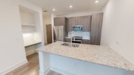 This well-appointed one-bedroom, two-bathroom residence at 350 Village Dr in King of Prussia, Pennsylvania offers a thoughtfully designed single-floor layout with modern finishes throughout. The open-concept kitchen serves as the heart of the home, showcasing floor-to-ceiling dark wood cabinetry, a sleek subway tile backsplash, and a generous granite-topped island with a double undermount sink and a professional-style pull-down faucet. Stainless steel appliances, including a French door refrigerator, built-in microwave, and range, complete the kitchen's contemporary aesthetic. Wood-look luxury flooring flows seamlessly throughout the living areas, adding warmth and continuity to the space. The bedroom is comfortably sized, featuring a ceiling fan, a window with an outdoor view, and direct access to a closet and the bathrooms. Both bathrooms are finished with granite vanity countertops and wood-toned cabinetry. One bathroom includes a soaking tub and shower combination enclosed by large-format marble-look tile. Recessed lighting throughout and crisp white walls create a bright, clean ambiance. A built-in shelving nook adds a refined architectural touch to the living area, rounding out this efficient and modern residence.