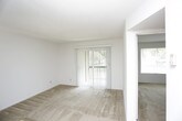 This single-story space is designed with a straightforward, functional layout that maximizes usability throughout. The entry area opens into a generously sized living room finished with wall-to-wall beige carpeting and white walls, creating a clean, neutral backdrop. A front entry door with an adjacent window allows natural light to filter into the space, while a sliding glass door on the opposite end of the living area provides direct access to the outdoors and frames views of surrounding greenery.

The galley-style kitchen runs along two parallel walls and features dark wood cabinetry on both sides, offering ample upper and lower storage. Light-colored countertops contrast the rich cabinetry tones, and the kitchen is equipped with a white electric range, refrigerator, and a double sink. Tile-style flooring lines the kitchen, and a window provides natural light to the workspace.

The bedroom is well-proportioned, with carpeted floors, a large window admitting outdoor views, and two side-by-side closets offering generous built-in storage. A textured ceiling is consistent throughout the home.

The bathroom includes a vanity with a dark wood cabinet base, a mirrored medicine cabinet, tile-style flooring, and a full bathtub and shower combination, completing this practical and well-organized space.