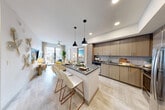 Located at 1050 Blanche St in West Palm Beach, FL, this well-appointed 2-bedroom, 2-bathroom residence offers a thoughtfully designed single-floor layout with modern finishes throughout. The open-concept kitchen, dining, and living area serves as the heart of the home, anchored by a center island with a dark quartz countertop and seating for two beneath sleek black pendant lights. The kitchen features light wood cabinetry extending to the ceiling, a classic subway tile backsplash, and stainless steel appliances. Light-toned tile flooring flows seamlessly through the main living areas, enhancing the bright, airy atmosphere. The living room opens to a private balcony offering elevated views of a resort-style pool deck lined with palm trees. The primary bedroom is a comfortable retreat with plush carpeting, a natural light-filled window, and generous closet space. The second bedroom features a ceiling fan, a tray ceiling detail, and a vibrant accent wall. Both bathrooms are finished with wood-toned vanities and stone countertops — the primary bath includes a glass-enclosed walk-in shower with a backlit mirror, while the second bath offers a clean, functional design. Additional conveniences include an in-unit laundry area and a dedicated entrance.