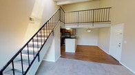 This two-story loft-style residence offers a thoughtfully designed layout that balances open living spaces with private retreats. The main floor centers around an open-concept living area finished with warm hardwood-style flooring, anchored by a cozy fireplace and a sliding glass door that opens to a private balcony overlooking lush outdoor greenery. Soaring vaulted ceilings and a striking open-railing staircase lend the space a sense of height and openness.

The kitchen is well-appointed with warm wood cabinetry, dark granite-style countertops, stainless steel appliances including a refrigerator, range, and microwave, as well as a double-basin sink and a breakfast bar peninsula that connects seamlessly to the dining and living areas.

Upstairs, the loft-style upper level overlooks the main living space below, adding to the home's airy, open feel. The bedrooms are generously sized, featuring plush carpeting and multiple windows that invite natural light and outdoor views. A bathroom features a dark granite-topped vanity with an undermount sink, complemented by neutral-toned textured walls. Throughout, the warm beige color palette and clean finishes create a welcoming and cohesive ambiance.