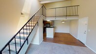 This two-story loft-style residence offers a thoughtfully designed layout that balances open living spaces with private retreats. The main floor centers around an open-concept living area finished with warm hardwood-style flooring, anchored by a cozy fireplace and a sliding glass door that opens to a private balcony overlooking lush outdoor greenery. Soaring vaulted ceilings and a striking open-railing staircase lend the space a sense of height and openness.

The kitchen is well-appointed with warm wood cabinetry, dark granite-style countertops, stainless steel appliances including a refrigerator, range, and microwave, as well as a double-basin sink and a breakfast bar peninsula that connects seamlessly to the dining and living areas.

Upstairs, the loft-style upper level overlooks the main living space below, adding to the home's airy, open feel. The bedrooms are generously sized, featuring plush carpeting and multiple windows that invite natural light and outdoor views. A bathroom features a dark granite-topped vanity with an undermount sink, complemented by neutral-toned textured walls. Throughout, the warm beige color palette and clean finishes create a welcoming and cohesive ambiance.