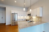 This thoughtfully designed two-bedroom, one-bathroom residence in Natick, MA offers a clean, modern aesthetic throughout its single-floor layout. The open-concept living, dining, and kitchen area serves as the heart of the home, anchored by warm hardwood flooring and an abundance of natural light. The kitchen is a standout, showcasing a large center island with elegant granite countertops, white shaker-style cabinetry with matte black hardware, a subway tile backsplash, and a full suite of stainless steel appliances including a refrigerator, range, microwave, and dishwasher. Pendant lighting above the island adds a polished finishing touch. The living area flows seamlessly from the kitchen, offering an open and airy feel. Both bedrooms are carpeted and bathed in natural light through generously sized windows that offer views of the surrounding Natick neighborhood. Three closets provide ample storage throughout. The bathroom features a glass-enclosed walk-in shower with mosaic tile flooring, a white vanity with a clean quartz countertop, and a large mirror. An in-unit laundry area adds everyday convenience. The overall palette of crisp whites and neutral tones creates a bright, contemporary atmosphere throughout.