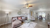 This single-floor residence offers a thoughtfully designed layout that balances comfort and functionality. The living room serves as the heart of the home, featuring crown molding, a ceiling fan with light fixture, hardwood-style flooring, and a chair rail that adds a classic architectural detail to the neutral gray walls. Natural light fills the space, creating a bright and welcoming ambiance.

The dining room is positioned adjacent to the living area and benefits from large sliding glass doors dressed with vertical blinds, allowing abundant natural light to pour in. A pendant light fixture hangs above the round dining table, and crown molding continues the refined aesthetic seen throughout the common areas.

The kitchen is equipped with white cabinetry, granite-style countertops, and full-size appliances including a black refrigerator, maintaining a clean and practical workspace.

The primary bedroom offers plush carpeting, a window with curtain panels, and ample space for substantial furniture. A second bedroom mirrors this comfortable design with soft carpeting, neutral walls, and natural light, providing a cheerful and restful retreat. Both bedrooms offer a calm, private atmosphere well-suited for rest and relaxation. Overall, the home presents a cohesive, move-in-ready aesthetic with consistent finishes and a warm, inviting character throughout.