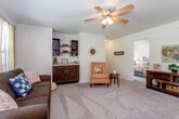 This single-floor residence in Topeka, Kansas offers a thoughtfully designed layout with comfortable living spaces throughout. The spacious living room is anchored by a ceiling fan, plush carpeting, and large windows that invite natural light and outdoor views. Built-in dark cabinetry with open shelving provides both storage and display space, adding a stylish touch to the room's warm ambiance.

The galley-style kitchen is well-equipped with dark espresso cabinetry, stainless steel appliances including a refrigerator and range, a double-basin sink, and durable wood-look flooring. A convenient pass-through connects the kitchen to the living and dining areas, promoting an open, connected flow.

The residence includes multiple bedrooms, each featuring soft carpeting, natural light from windows with blinds and curtains, and ample space for furnishings. The primary bedroom includes direct access to a private bathroom, complete with dark cabinetry, a stone-topped vanity, a large mirror, and a tub/shower combination.

A second bathroom mirrors the refined finishes found throughout, featuring matching dark cabinetry and a stone-finish countertop. The consistent use of dark wood tones, neutral walls, and quality finishes creates a cohesive and inviting atmosphere across the entire space.