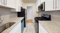 This single-floor residence offers a thoughtfully updated interior with a clean, modern aesthetic carried consistently throughout. The galley-style kitchen is a functional highlight, featuring white shaker cabinetry with brushed nickel hardware, light granite countertops, and a white subway tile backsplash. It is equipped with stainless steel appliances, including an over-the-range microwave and gas range, alongside a black refrigerator and dishwasher. Light tile flooring completes the kitchen's polished look, and an open doorway connects the space to the rest of the unit.

The bathroom continues the modern palette with white cabinetry, a marble-look granite vanity top, and matching light tile flooring. A tub-shower combination enclosed by sliding glass doors provides a clean, streamlined appearance.

The living areas are defined by warm, honey-toned hardwood floors that extend throughout, lending continuity and brightness to each room. The open living space features a partial dividing wall that subtly separates areas while maintaining an airy feel. A front entry door with a sidelight panel allows natural light to flow in. The bedroom offers a wide sliding closet and access to an additional storage area, completing this well-maintained and move-in ready residence.