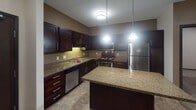 Located at 1290 County Road F W in Arden Hills, Minnesota, this single-floor residence offers a thoughtfully designed layout with consistent, modern finishes throughout. The kitchen serves as a central highlight, featuring rich dark-wood cabinetry, granite countertops, a central island with pendant lighting, and a full suite of stainless steel appliances including a refrigerator, range, built-in microwave, and dishwasher. Tile flooring completes the kitchen's polished look.

The living and bedroom areas are finished with wall-to-wall carpeting and neutral-toned walls, creating a warm and cohesive atmosphere. Multiple bedrooms offer ceiling fans, windows with natural light, and access to closet space, while baseboard heating ensures comfort year-round. An in-unit stacked washer and dryer adds everyday convenience.

The bathroom is well-appointed with dark wood vanity cabinetry, granite countertops, an undermount sink, a large mirror with overhead lighting, and tile flooring. A second bathroom mirrors this refined aesthetic. Dark-trimmed doorways and consistent hardware choices tie the design together, giving the entire space a unified, contemporary feel with functional, practical living in mind.
