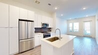 This well-appointed 1-bedroom, 1-bathroom residence offers a thoughtfully designed single-level layout that maximizes both function and comfort. The open-concept living and kitchen area is anchored by a sleek kitchen featuring floor-to-ceiling white cabinetry, a dark subway tile backsplash, stainless steel appliances including a French door refrigerator, microwave, and range, and a central island with a light quartz countertop and undermount sink. Light wood-look flooring runs throughout the main living areas, enhancing the bright, airy atmosphere created by recessed lighting and large windows. The living room opens directly to a private balcony through a glass door, allowing natural light to pour in and providing outdoor views. The bedroom is a comfortable, carpeted retreat with dual windows that frame exterior views and include a ceiling fan fixture. It connects conveniently to a dedicated closet and the full bathroom, which features white subway tile surround, a soaking tub, a vanity, and in-unit stacked washer and dryer. The overall design palette of crisp whites and neutral tones gives the space a clean, modern aesthetic throughout.