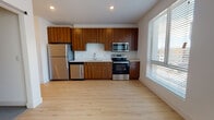 This single-floor unit showcases a contemporary design with a cohesive blend of warm wood tones, crisp white walls, and light hardwood-style flooring that runs throughout the main living areas. The open kitchen is a standout feature, equipped with a full suite of stainless steel appliances including a refrigerator, electric range, over-the-range microwave, and dishwasher. Rich, wood-grain cabinetry extends from floor to ceiling, complemented by clean white countertops and recessed lighting overhead. A large window adjacent to the kitchen floods the space with natural light and offers views of the surrounding neighborhood.

The living area is bright and open, enhanced by a ceiling fan and a bank of wide windows fitted with horizontal blinds. The bedroom is a generously sized, carpeted retreat featuring ample closet space with dual sliding-door closets and access to additional natural light. A secondary room with hardwood-style flooring provides flexible use as a bedroom or office.

The bathroom maintains the unit's modern aesthetic with a wood-vanity cabinet, white quartz countertop, undermount sink, and a full soaking tub with shower combination set against clean white walls and light flooring.