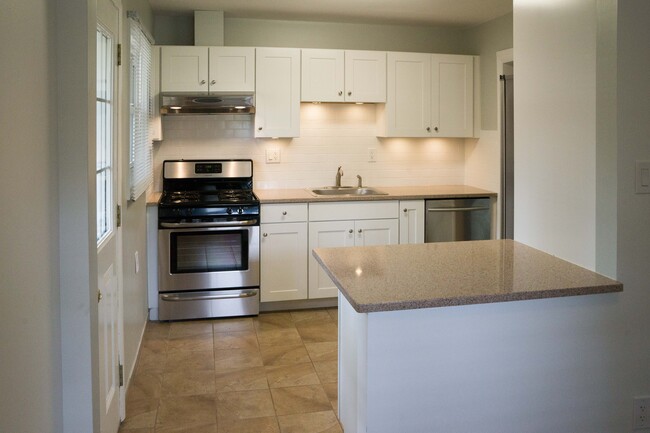 Kitchen features stainless steel appliances, quartz countertops and tile floor. Also partially shown in foreground is breakfast nook or dining area. - 2040 Arlington Ave NE