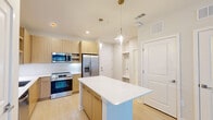 Located at 1224 Old Peachtree Rd NE in Lawrenceville, GA, this well-designed one-bedroom, one-bathroom residence offers a thoughtfully organized single-floor layout with modern finishes and a bright, airy ambiance throughout.

The kitchen serves as the centerpiece of the open-concept living area, featuring light wood cabinetry, a white quartz countertop island with pendant lighting overhead, a white subway tile backsplash, and a full suite of stainless steel appliances including a French door refrigerator, range, built-in microwave, and dishwasher. The kitchen flows seamlessly into the living area, which benefits from natural light streaming through large windows fitted with horizontal blinds, and is equipped with a ceiling fan.

The bedroom is a comfortable, well-proportioned retreat with light hardwood-style flooring, neutral wall tones, a ceiling fan, and a window offering outdoor views. An adjacent walk-in closet provides generous storage with multi-tiered wire shelving systems.

The bathroom is elegantly appointed with a dual-sink wood vanity, white quartz countertops, framed mirrors, pendant sconce lighting, and marble-style tile accents. Light hardwood-style flooring runs consistently throughout the entire residence, contributing to its cohesive, contemporary character.
