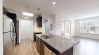 This thoughtfully designed 1-bedroom, 1-bathroom residence offers a functional and modern layout across a single floor. The open-concept kitchen and living area serves as the heart of the home, featuring light hardwood-style flooring, recessed lighting, and a skylight that fills the space with natural light. The kitchen is equipped with dark espresso cabinetry, granite countertops, a central island with a built-in sink, and stainless steel appliances including a refrigerator and dishwasher. The living area extends naturally from the kitchen, offering large windows with outdoor views and access to a balcony, creating a bright and airy atmosphere. The bedroom is a comfortable, carpeted retreat with dual windows, a ceiling fan, and ample natural light. A walk-in closet with wire shelving provides generous storage. The bathroom features large-format tile, a soaking tub with a tiled shower surround, a granite-topped vanity, and a sleek chrome heated towel rack. A dedicated in-unit laundry area with a full-size washer and dryer adds everyday convenience. Clean white walls and consistent finishes throughout lend the space a cohesive, modern aesthetic.