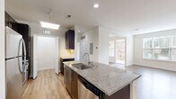 This thoughtfully designed 1-bedroom, 1-bathroom residence offers a functional and modern layout across a single floor. The open-concept kitchen and living area serves as the heart of the home, featuring light hardwood-style flooring, recessed lighting, and a skylight that fills the space with natural light. The kitchen is equipped with dark espresso cabinetry, granite countertops, a central island with a built-in sink, and stainless steel appliances including a refrigerator and dishwasher. The living area extends naturally from the kitchen, offering large windows with outdoor views and access to a balcony, creating a bright and airy atmosphere. The bedroom is a comfortable, carpeted retreat with dual windows, a ceiling fan, and ample natural light. A walk-in closet with wire shelving provides generous storage. The bathroom features large-format tile, a soaking tub with a tiled shower surround, a granite-topped vanity, and a sleek chrome heated towel rack. A dedicated in-unit laundry area with a full-size washer and dryer adds everyday convenience. Clean white walls and consistent finishes throughout lend the space a cohesive, modern aesthetic.