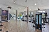 Located at 83 Ernest W Barrett Pkwy NW in Marietta, Georgia, this well-appointed fitness center offers a comprehensive workout environment designed for both functionality and comfort. The single-floor facility features warm wood-look flooring throughout, white structural columns, and ceiling fans that contribute to a bright, airy atmosphere.

The cardio zone is a standout feature, lined with floor-to-ceiling windows that flood the space with natural light and offer direct views of the outdoor pool area and surrounding greenery. Multiple treadmills, upright stationary bikes, and elliptical machines are positioned to take full advantage of these scenic outdoor views.

A dedicated strength training area anchors one side of the facility, featuring a multi-functional cable machine, weight bench, and strength equipment. Bold blue accent walls define this zone and add a dynamic contrast to the clean white trim and light flooring. A wall-mounted television provides entertainment during workouts.

An alcove area, highlighted with deep purple accent walls, houses a water station with cabinetry, providing convenient hydration access. Adjacent to this, a well-stocked rack of colorful kettlebells and a full-length mirror support free weight and functional training workouts. A separate area accommodates stability balls and resistance accessories, rounding out the facility's versatile offerings. The overall ambiance is energetic yet inviting, catering to a wide range of fitness needs.
