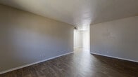 This single-floor unit offers a functional and straightforward layout, characterized by consistent dark hardwood-style flooring that runs throughout the main living areas, bedroom, kitchen, and bathroom. The living area is generously proportioned, featuring neutral-toned walls, a textured popcorn ceiling, and a wall-mounted HVAC vent. A connected secondary area, separated by a wide opening, features vertical blinds and provides additional flexible space. Arched windows in both the living area and bedroom allow natural light to fill the rooms, lending an airy quality to the interior.

The galley-style kitchen is efficiently designed with dark wood cabinetry, light countertops, a stainless steel sink, and black appliances including a refrigerator, range, and dishwasher. Light-toned hardwood-style flooring contrasts with the darker cabinetry, creating a clean visual balance.

The bedroom includes a ceiling fan with light fixture, an arched window with outdoor views, and a sizeable closet with double hanging rods offering ample storage. The bathroom features a tiled tub-shower combination, a dark wood vanity with a light countertop, and a large mirror.