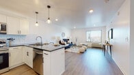 This single-floor residence is designed with a clean, modern aesthetic, characterized by white walls, recessed lighting, and light hardwood-style flooring that flows consistently throughout the space. The open-concept layout seamlessly connects the kitchen and living area, creating a functional and sociable environment.

The kitchen is well-equipped with stainless steel appliances, including a refrigerator, range, microwave, and dishwasher. White shaker-style cabinetry pairs with a classic subway tile backsplash and dark granite countertops. A peninsula with seating for multiple bar stools serves as a central gathering point, illuminated by stylish pendant lights overhead.

The living area is generously sized, featuring a large window that invites natural light and offers outdoor views. Recessed lighting supplements the natural light, keeping the space bright and welcoming.

The bedroom is a calm retreat with its own window providing natural light and outdoor views, complemented by light hardwood flooring and clean white walls.

The bathroom features wood-look tile flooring, a vanity with a mirror, and marble-style wall accents, contributing to the unit's consistently polished and contemporary character throughout.