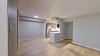 This single-floor unit offers a clean, modern aesthetic defined by neutral gray walls, light wood-tone laminate flooring, and white trim that runs consistently throughout every room. The open living area is generously proportioned, featuring recessed lighting and a built-in shelving unit flanked by two windows fitted with horizontal blinds, allowing natural light to fill the space comfortably.

The kitchen is designed in a galley layout with gray cabinetry, white quartz-style countertops, a subway tile backsplash, and stainless steel appliances including a refrigerator and dishwasher. A peninsula counter with a raised bar section connects the kitchen to the living area, providing a casual dining or workspace option. A set of double doors within the kitchen offers additional storage or pantry access.

The bedrooms are well-sized and share the same light flooring. One bedroom features a ceiling fan with integrated lighting and a window with blinds, while another includes recessed lighting and direct access to the bathroom area. The bathroom is thoughtfully divided, with a separate vanity space featuring gray cabinetry and a wide mirror, leading into a compartmentalized toilet and tub area clad in large-format gray tile.