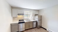 Located at 279 Amherst Rd in Sunderland, MA, this efficiently designed single-floor unit offers a thoughtful layout that maximizes its compact footprint. The main living area features light wood-style vinyl flooring that runs throughout, lending a clean and cohesive aesthetic to the space. Neutral-toned walls and ceiling-mounted lighting contribute to a bright, open feel.

The kitchen is a functional highlight of the unit, equipped with stainless steel appliances including a range, dishwasher, and refrigerator. Two-toned cabinetry — white uppers and gray lowers — pairs with a window above the sink that allows natural light to filter in, offering views of the surrounding landscape. A baseboard heating unit ensures warmth during cooler months.

A separate bedroom area provides a quiet retreat, complete with a louvered closet door for storage and its own baseboard heater. The neutral walls and consistent flooring maintain the unit's unified aesthetic.

The bathroom is clean and practical, featuring a white vanity, toilet, and a wall-mounted heater. A small window positioned high on the wall brings in natural light while maintaining privacy. Grab bars and a towel rack add functional detail to the space.

Overall, this unit presents a well-maintained, move-in ready layout suited for efficient, comfortable living.
