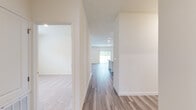This single-story home is designed with a clean, contemporary aesthetic and a practical layout that maximizes comfort throughout. The interior is finished in a neutral, warm palette with crisp white trim and walls that create a bright, cohesive feel across all areas.

The hallway serves as the central connector, featuring wood-look plank flooring that extends into the main living areas. The living room is generously proportioned, with recessed lighting, a window allowing natural light, and the same durable wood-look flooring underfoot.

The kitchen is a functional highlight, equipped with white shaker-style cabinetry, granite countertops with subtle grey veining, and a full suite of stainless steel appliances including a range, over-the-range microwave, dishwasher, and French door refrigerator. A kitchen island provides additional prep and counter space.

The bedrooms are carpeted for comfort, with windows fitted with blinds for light control. The primary bedroom connects to a well-sized bathroom featuring a dual-sink vanity, a walk-in shower with sliding glass doors, and direct access to a spacious walk-in closet. An additional bathroom includes a full soaking tub and shower combination with built-in shelving.