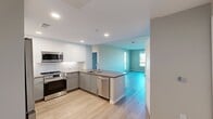 North Grove B2C is a well-appointed 3-bedroom, 2-bathroom residence spanning 1,050 square feet on a single floor in Riverside, CA. The open-concept living room features light gray wood-style flooring and neutral-toned walls, seamlessly connecting to the kitchen via a peninsula counter. The kitchen is outfitted with modern gray shaker cabinetry, stainless steel appliances including a refrigerator, range, and over-the-range microwave, white subway tile backsplash, and recessed lighting. The primary bedroom measures 140 square feet and includes large windows offering outdoor views and ample natural light, with durable wood-style flooring. The two additional bedrooms are carpeted and feature windows with exterior views and access to the hallway. Two closets provide additional storage throughout the unit. Both bathrooms include wood-style flooring, shaker-style vanity cabinetry with taupe countertops, large mirrors, and a shower-tub combo. The primary bath features a double-sink vanity. A central hallway connects all rooms efficiently. The entry area includes louvered closet doors and a keypad-secured front door, rounding out this clean, modern Riverside residence.