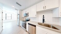 Located at 1701 N Florida Ave in Tampa, FL, this efficiently designed single-floor unit offers a clean, contemporary aesthetic throughout. The open-concept kitchen and living area serves as the heart of the space, featuring crisp white shaker cabinetry, light stone countertops, a textured tile backsplash, and a full suite of stainless steel appliances including an electric range, over-the-range microwave, dishwasher, and refrigerator. A matte black faucet adds a modern contrast to the bright, airy palette. Light wood-look flooring flows seamlessly throughout, reflecting the abundant natural light that pours in through large windows dressed with horizontal blinds, offering views of the surrounding greenery. The living area provides a bright, open canvas with white walls and a neutral tone that maximizes the sense of space. The full bathroom is thoughtfully appointed with hexagonal tile surrounding a soaking tub and shower combination, complemented by matte black fixtures and hardware for a cohesive, stylish finish. Three closets offer generous storage solutions, while a dedicated laundry area adds everyday convenience. The overall ambiance is fresh, bright, and move-in ready, with modern finishes that create a welcoming and functional living environment.