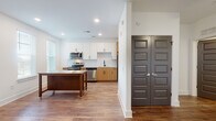 Located at 1290 Old Peachtree Rd NW in Duluth, Georgia, this well-appointed single-floor residence combines modern design with functional living. Throughout the space, warm hardwood-style flooring provides a cohesive and inviting foundation, complemented by crisp white walls and recessed lighting.

The kitchen stands out as a central highlight, showcasing a thoughtful two-tone cabinet design with white upper cabinetry and natural wood lower cabinets, accented by a classic white subway tile backsplash. Granite countertops and a full suite of stainless steel appliances — including a range, microwave, and dishwasher — round out this well-equipped cooking space. A freestanding island with a stainless steel top adds additional prep and gathering space, while large windows flood the area with natural light and offer pleasant outdoor views.

The living areas are open and airy, featuring ceiling fans and an abundance of natural light streaming through multiple windows with blinds. Bold gray double doors with raised panel detailing provide a striking architectural contrast against the neutral palette and lead to a generous closet space.

The bathroom is clean and bright, featuring a full tub-shower combination with white tile surround and brushed nickel fixtures. A connecting hallway with recessed lighting ties the layout together seamlessly, creating a comfortable and cohesive living environment.