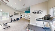 Located at 10010 Skinner Lake Dr in Jacksonville, FL, this fitness center offers a well-rounded exercise environment designed to support a variety of workout routines. The space is thoughtfully laid out across a single floor, providing ample room for both cardio and strength training activities.

Architecturally, the facility features soaring vaulted ceilings in the main workout area, accented by recessed lighting and ceiling fans that promote airflow and comfort during workouts. A striking arched window allows natural light to flood the space, complementing the neutral, light-toned walls and durable carpeted flooring. A bold teal accent wall adds a vibrant pop of color, while motivational wall decals — including "Discipline Beats Motivation" — contribute to an energizing atmosphere.

The cardio section is well-stocked with treadmills, elliptical trainers, a stationary bike, and a stair climber, all positioned near windows offering views of the outdoors. The strength training area includes a cable machine, adjustable weight benches, a rack of dumbbells, and an assortment of exercise balls. Wall-mounted mirrors expand the sense of space and allow users to monitor their form. A wall-mounted television provides entertainment during workouts. The combination of natural light, high ceilings, and diverse equipment makes this fitness center a comprehensive and inviting space for residents.