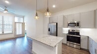 This thoughtfully designed 3-bedroom, 2-bathroom single-floor residence combines modern aesthetics with functional living. The open-concept kitchen serves as the heart of the home, featuring granite countertops, a central island with elegant geometric pendant lighting, gray shaker-style cabinetry, a white subway tile backsplash, and a full suite of stainless steel appliances including a French door refrigerator, electric range, microwave, and dishwasher. A built-in desk nook near the entry adds a practical workspace element. Wood-style plank flooring flows throughout the main living areas, contributing to a warm, cohesive feel. The bedrooms are bright and generously proportioned, with large windows that admit natural light and offer views of the surrounding community. The primary suite includes a spacious walk-in closet with built-in shelving and double hanging rods. The primary bathroom is outfitted with a dual-sink granite vanity, framed mirrors, and a walk-in shower. The secondary bathroom features marble-look tile flooring and wall surround, a soaking tub, and a granite vanity. Clean white walls and recessed lighting throughout lend the home a crisp, contemporary ambiance.
