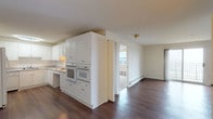 Unit 812 is a single-floor, 1-bedroom, 1-bathroom residence offering a clean, functional layout with a bright and neutral color palette throughout. The living area is generously sized, featuring rich dark hardwood-style flooring, baseboard heating, and multiple closets for additional storage. Natural light filters in through windows, creating a welcoming atmosphere. The kitchen is well-appointed with white shaker-style cabinetry, tile backsplash, light countertops, and a full suite of white appliances including a cooktop, double wall ovens, dishwasher, and refrigerator. The layout offers an efficient U-shaped design with ample counter and cabinet space. The bedroom is carpeted for comfort, features a ceiling fan, a window with outdoor views, and an impressive wall of closets with mirrored sliding doors providing generous storage capacity. The bathroom is equipped with a full tub and shower combination, white tile flooring, and accessibility features including grab bars. Throughout the unit, baseboard heating and wall-unit air conditioning ensure year-round comfort. The overall ambiance is clean, practical, and move-in ready.