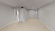 Unit #18 is a two-bedroom, one-bathroom single-floor residence offering a well-organized layout with a clean, contemporary aesthetic. Throughout the unit, light-toned wood-look flooring creates a cohesive and airy feel, complemented by soft gray walls and crisp white trim.

The living area features a front entry door with a transom window alongside a large window fitted with blinds, allowing ample natural light to fill the space. Recessed lighting provides additional illumination throughout.

The kitchen is efficiently designed with white shaker-style cabinetry, granite-patterned countertops, a subway tile backsplash, open wood shelving, and stainless steel appliances including a gas range and refrigerator.

Both bedrooms are comfortably sized with neutral finishes and natural light from windows with blinds. One bedroom includes a closet with built-in shelving. The second bedroom features an open, flexible layout.

The bathroom is clean and functional, featuring a full tub/shower combination with white tile surround, a window for natural light, and standard fixtures. The unit also includes closet storage and a HVAC vent system for climate control.