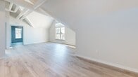 Located at 344 Driftway in Scituate, Massachusetts, this thoughtfully designed single-floor unit offers a clean, modern aesthetic throughout its well-proportioned layout. The space is defined by striking vaulted and cathedral ceilings that lend an airy, expansive quality to multiple rooms, complemented by an abundance of natural light streaming through generously sized windows that frame views of the surrounding neighborhood.

Light-toned hardwood flooring runs continuously throughout the unit, creating a cohesive and polished look. The kitchen is a standout feature, showcasing floor-to-ceiling white shaker cabinetry, a textured tile backsplash, dark countertops, stainless steel appliances including a range, microwave, and refrigerator, and a movable island with additional workspace. High clerestory windows above the cabinetry amplify the sense of volume and light in this area.

The living and sleeping areas benefit from the dramatic ceiling heights, with angled rooflines adding architectural character. A spacious walk-in closet with built-in wire shelving provides practical storage. The bathroom is finished with wood-look tile flooring, a glass-enclosed shower, and a vanity with drawer storage, maintaining the unit's clean, contemporary character throughout.