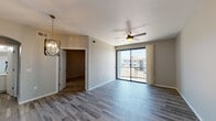 This single-floor residence offers a clean, contemporary design with a cohesive neutral color palette throughout. The open living area is finished with durable wood-look plank flooring in a cool gray tone, complemented by a ceiling fan and an elegant multi-bulb chandelier that adds a modern accent. A full-width sliding glass door leads to a private balcony, allowing natural light to fill the space and providing views of the surrounding community. An arched doorway connects the living area to a well-lit bathroom, which features white shaker-style cabinetry with matte black hardware, a single undermount sink, and a large frameless mirror. The kitchen is thoughtfully outfitted with crisp white cabinetry, quartz countertops, a gray subway tile backsplash, and a full suite of stainless steel appliances including a refrigerator, range, and over-the-range microwave. The bedroom is carpeted for comfort, benefits from a ceiling fan, and receives natural light through a large window with exterior views. A spacious closet is conveniently accessible from the main living area. A programmable smart thermostat is also present, adding a practical modern touch to this well-designed residence.