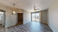 This single-floor residence offers a clean, contemporary design with a cohesive neutral color palette throughout. The open living area is finished with durable wood-look plank flooring in a cool gray tone, complemented by a ceiling fan and an elegant multi-bulb chandelier that adds a modern accent. A full-width sliding glass door leads to a private balcony, allowing natural light to fill the space and providing views of the surrounding community. An arched doorway connects the living area to a well-lit bathroom, which features white shaker-style cabinetry with matte black hardware, a single undermount sink, and a large frameless mirror. The kitchen is thoughtfully outfitted with crisp white cabinetry, quartz countertops, a gray subway tile backsplash, and a full suite of stainless steel appliances including a refrigerator, range, and over-the-range microwave. The bedroom is carpeted for comfort, benefits from a ceiling fan, and receives natural light through a large window with exterior views. A spacious closet is conveniently accessible from the main living area. A programmable smart thermostat is also present, adding a practical modern touch to this well-designed residence.