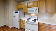 Located at 1919 Spring Garden St in Greensboro, NC, this single-floor residence offers a well-organized layout designed for comfortable everyday living. The kitchen is efficiently appointed with warm honey-toned wood cabinetry providing ample storage, white appliances including a coil-top electric range, over-the-range microwave, refrigerator, and a sink with a countertop peninsula that opens toward the living area. The flooring in the kitchen transitions to rich, dark hardwood-style planks, adding a grounded contrast to the neutral walls throughout. The open living area extends generously from the kitchen, featuring plush wall-to-wall carpeting, and is filled with natural light from multiple windows. Multiple bedrooms are each fitted with soft carpeting, ceiling fans with light fixtures, and windows that bring in views of the surrounding greenery. The bathrooms feature tub-shower combinations, wood-toned vanity cabinetry, and durable hardwood-style flooring. Textured ceilings are consistent throughout the unit, and neutral warm-toned walls create a cohesive, understated atmosphere. The thoughtful floor plan, visible in the dollhouse view, highlights a clear separation between living and private spaces, making this a practical and comfortable residence.