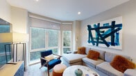 Located at 95 Saint Alphonsus St in Boston's Mission Hill neighborhood, this single-floor residence offers a thoughtfully designed layout with modern finishes throughout. The living room is a standout space, anchored by corner windows that flood the room with natural light and frame lush greenery views. Light hardwood flooring, recessed lighting, and a bold abstract wall piece contribute to the contemporary aesthetic.

The kitchen is well-appointed with a two-tone cabinet scheme—white uppers contrasting rich dark lowers—complemented by dark granite countertops, a striking blue tile backsplash, and a full suite of stainless steel appliances. A granite-topped island provides additional workspace and casual dining potential, while a pendant light adds a refined finishing touch.

The space includes two bedrooms, each featuring light hardwood floors, soft neutral tones, and ample natural light. One bedroom benefits from a large window with sheer drapery, enhancing the airy feel. Both rooms are well-proportioned and offer a calm, restful atmosphere.

The bathroom is finished with dark tile flooring, a white quartz vanity countertop, and a tub-shower combination. Clean lines and neutral tones keep the space feeling crisp and functional. Overall, this residence presents a polished, contemporary living environment in one of Boston's vibrant urban neighborhoods.