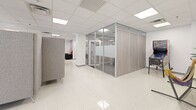 Located at 220 E Madison St in the heart of downtown Tampa, this expansive single-floor commercial office space delivers a thoughtfully designed environment built for productivity, collaboration, and creativity. The layout balances open-plan work areas with defined private zones, all unified by gleaming terrazzo flooring and a bright, white drop-tile ceiling with recessed panel lighting throughout.

The open workstation areas feature modular benching desks and ergonomic seating, bathed in natural light from large windows that frame views of Tampa's lush greenery and urban skyline. A dedicated breakroom station with coffee service and snack vending offers convenient amenities for occupants.

Glass-walled partitions with frosted accents divide the space into sleek private offices and a dedicated conference room, maintaining visual openness while providing acoustic separation. Wide corridors are punctuated by tall potted plants and bold accent walls, lending warmth to the contemporary design.

Collaborative lounge zones are furnished with striking red and gray modular seating arrangements, ideal for informal meetings or social gatherings. A standout feature is the dedicated screening room, appointed with black walls, dramatic red and black curtains, leather reclining sofas, and large-screen display technology — offering a fully immersive media experience. This versatile office suite is well-suited for a dynamic, modern organization.