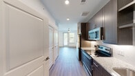 This single-floor residence offers a well-designed layout with contemporary finishes throughout. The kitchen is a standout feature, equipped with a full suite of stainless steel appliances including an electric range, over-the-range microwave, refrigerator, and dishwasher. Rich dark brown cabinetry provides ample storage, complemented by light granite countertops and a herringbone-patterned tile backsplash. A single-basin sink with a modern faucet completes the functional workspace.

Wood-style plank flooring runs continuously throughout the unit, lending warmth and cohesion to the open layout. The living area benefits from generous natural light provided by large windows fitted with blinds, and a ceiling fan with a light fixture serves the space efficiently. Recessed lighting is installed throughout, adding to the bright, clean ambiance.

The bathroom features a dark vanity cabinet paired with a granite countertop, a wide mirror with overhead lighting, and wood-style flooring that maintains consistency with the rest of the unit. A windowed view from the bathroom connects visually to an adjacent room, enhancing the sense of openness.

Additional features include white panel interior doors, a utility panel, and closet storage. The overall design is modern, clean, and functional.