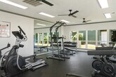 This dedicated fitness room offers a thoughtfully organized workout space designed to support a well-rounded exercise routine. The room features durable rubber flooring throughout, providing a safe and functional surface for a wide range of activities. Large windows line the walls, flooding the space with natural light and offering views of the surrounding outdoor areas, while multiple ceiling fans ensure consistent airflow and comfort during workouts. A full-length wall mirror enhances the sense of openness and allows users to monitor their form. The cardio section is well-stocked with treadmills, an elliptical trainer, a stationary bike, and rowing machines, all from the Spirit brand. Strength training options include a multi-function power tower for bodyweight exercises and a comprehensive dumbbell rack with a wide range of free weights. A beverage vending machine is conveniently located within the room for post-workout hydration. Overhead fluorescent lighting supplements the natural light, keeping the space bright at all hours. Motivational wall art adds an energizing touch to the clean, white-painted interior. French doors on one side of the room provide direct access to the outdoor area, enhancing the connection between the fitness facility and its surroundings.