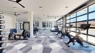 Located at 2124 American Industrial Way in Chamblee, GA, this fitness center is a well-appointed, single-floor exercise facility offering a generous and open layout designed to accommodate a wide range of workout activities. The space is defined by its modern, contemporary aesthetic, featuring a striking geometric-patterned carpet in varying shades of gray that adds visual depth and dynamism to the floor.

Natural light floods the interior through large, black-framed floor-to-ceiling windows and two full-width glass garage doors that open to exterior views, creating an airy and energizing atmosphere. Ceiling fans are distributed throughout, complementing the recessed and flush-mount gold-accented lighting fixtures overhead.

The cardio zone, positioned near the glass garage doors, houses treadmills and stationary cycling bikes. The strength training area features a multi-functional cable machine, free weight racks with dumbbells, adjustable benches, and a squat/power rack. Full-length mirrors framed in exposed brick accent walls provide functional and decorative contrast against the otherwise clean white walls and structural columns.

Built-in shelving offers organized storage for smaller equipment and accessories. The facility also includes a dedicated stretching and functional training area, offering ample open floor space. The overall design balances industrial character with modern finishes, creating a motivating and professional training environment.