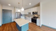 Located at 1325 Utica Ave S in St. Louis Park, MN, this thoughtfully designed single-floor residence combines contemporary finishes with functional living spaces. The kitchen serves as the heart of the home, showcasing crisp white shaker cabinetry, a herringbone tile backsplash, light quartz countertops, and a full suite of stainless steel appliances including a refrigerator, electric range, over-the-range microwave, and dishwasher. A teal-accented center island with a smooth white surface provides additional prep space and casual seating, while globe pendant lights lend a warm, modern ambiance. The kitchen flows naturally into the living area, where wood-look flooring and large windows invite ample natural light and open views of the surrounding urban landscape. The bedroom features plush carpeting and a generous picture window that frames views of the neighboring architecture and sky above. The bathroom is efficiently designed with a wood-framed vanity mirror, clean white fixtures, and convenient access to an in-unit stacked washer and dryer. Throughout the residence, a cohesive neutral palette with teal accent details and modern lighting creates a polished, move-in-ready atmosphere well-suited to contemporary urban living.