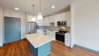 Located at 1325 Utica Ave S in St. Louis Park, MN, this thoughtfully designed single-floor residence combines contemporary finishes with functional living spaces. The kitchen serves as the heart of the home, showcasing crisp white shaker cabinetry, a herringbone tile backsplash, light quartz countertops, and a full suite of stainless steel appliances including a refrigerator, electric range, over-the-range microwave, and dishwasher. A teal-accented center island with a smooth white surface provides additional prep space and casual seating, while globe pendant lights lend a warm, modern ambiance. The kitchen flows naturally into the living area, where wood-look flooring and large windows invite ample natural light and open views of the surrounding urban landscape. The bedroom features plush carpeting and a generous picture window that frames views of the neighboring architecture and sky above. The bathroom is efficiently designed with a wood-framed vanity mirror, clean white fixtures, and convenient access to an in-unit stacked washer and dryer. Throughout the residence, a cohesive neutral palette with teal accent details and modern lighting creates a polished, move-in-ready atmosphere well-suited to contemporary urban living.