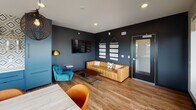 Located at E 18th St in Minneapolis, this single-floor space offers a thoughtfully designed interior that blends bold aesthetics with functional versatility. The open layout connects a fully equipped kitchenette, a generous dining area, and a relaxed lounge zone, all unified by warm hardwood-style flooring throughout.

The kitchenette is a standout feature, distinguished by vivid cobalt-blue cabinetry, a geometric diamond-patterned tile backsplash, open wood shelving, a white countertop with an undermount sink, and a built-in microwave. The design is both visually striking and practical.

The dining area centers on a large, light-toned reclaimed wood table surrounded by rust-orange chairs. Overhead, sculptural wire pendant lights add a dramatic, artistic touch. Floor-to-ceiling windows and sliding glass doors flood the space with natural light and frame sweeping views of the Minneapolis skyline, with direct access to a spacious outdoor terrace furnished for gathering and relaxation.

The lounge area features deep charcoal walls, a tufted caramel leather sofa, a teal velvet accent chair, a wall-mounted television, and a brass floor lamp, creating an intimate yet contemporary atmosphere.