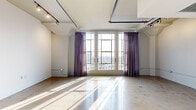 Located in the heart of Downtown Los Angeles at 819 Santee St, this one-bedroom, one-bathroom loft delivers a compelling blend of industrial character and modern finishes. The main living area is anchored by polished concrete floors that reflect natural light streaming through large, floor-to-ceiling windows dressed with sheer purple curtains, offering sweeping city views. Exposed ceiling pipes and overhead track lighting underscore the unit's industrial aesthetic, while white walls keep the space feeling open and bright.

The kitchen is well-appointed with light wood cabinetry extending to the ceiling for generous storage, a blue mosaic tile backsplash, stainless steel appliances including a refrigerator with built-in ice maker, electric range, microwave, and dishwasher, all set against clean countertops. A structural column adds an architectural focal point to the kitchen area.

The bathroom features large-format gray tile flooring, a sleek glass-enclosed soaking tub and shower combination with a dark stacked mosaic tile surround, and floor-to-ceiling wood-paneled storage cabinetry. A bold orange entry door and a glass-paned interior door further accent the loft's distinctive industrial-modern design throughout.