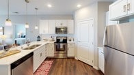 This single-floor residence offers a thoughtfully designed layout with multiple bedrooms, well-appointed bathrooms, and a modern kitchen that serves as a central hub of the home. The kitchen stands out with its crisp white cabinetry, subway tile backsplash, quartz countertops, and a full suite of stainless steel appliances, including a refrigerator, range, microwave, and dishwasher. Pendant lighting illuminates a breakfast bar with seating, adding a casual dining option to the space.

The bedrooms are carpeted and finished in warm neutral tones, each featuring windows with blinds that allow natural light while maintaining privacy. The primary bedroom connects to a private en-suite bathroom equipped with a granite-topped vanity, white cabinetry, and hardwood-style flooring. A second bathroom mirrors this aesthetic, also featuring a granite countertop vanity and a shower with a curtain enclosure.

Throughout the residence, hardwood-style flooring is present in the kitchen and bathrooms, while plush carpet runs through the bedrooms. The overall palette of soft grays and warm beiges, paired with recessed and pendant lighting, creates a cohesive and comfortable living environment suited for everyday functionality.